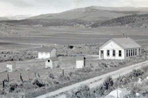 A black and white photo of the school slightly distant on the right with rolling hills and plains around it.