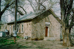 A view of the school with gabled roof and red door below. On either side and behind are some leafless trees. 