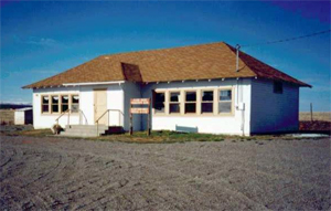 A picture of the school with hipped roof and white walls with a row of windows on either side of the protruding entrance.