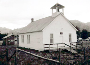 A photo of the school with white walls and overhanging gabled roof beneath a bell tower in black and white.