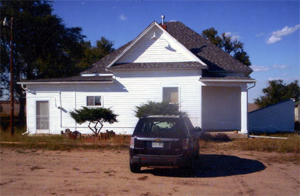 A view of the white school with gable roof and hipped roof behind it and extension going out to the left side. In front of the building is a van. 